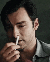 a man is holding a cigarette in his hand and blowing it out of his nose .