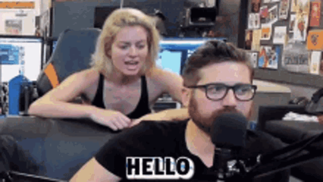 a man and a woman are sitting in front of a microphone . the man is saying hello .
