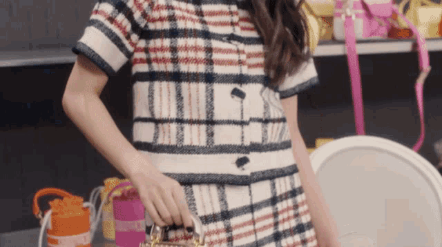 a woman in a plaid dress is holding a pink purse