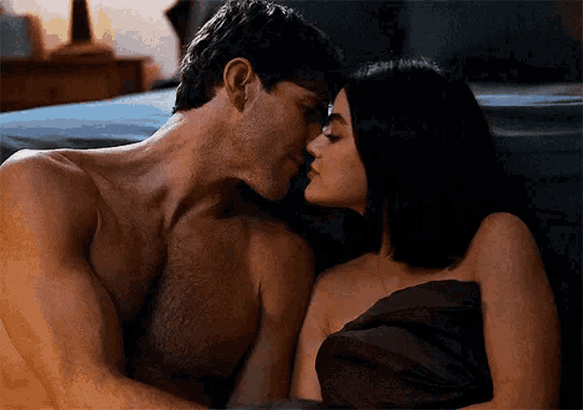 a man and a woman are kissing in bed . the man is shirtless and the woman is naked .