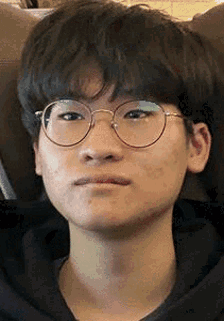 a young man wearing glasses and a black hoodie is sitting on a chair .