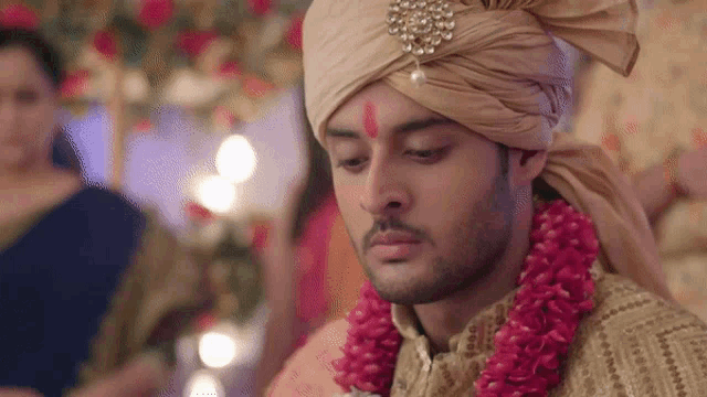the groom is wearing a turban and a garland of flowers around his neck .