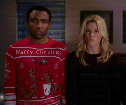 a man in a merry christmas sweater points at a woman in a black shirt