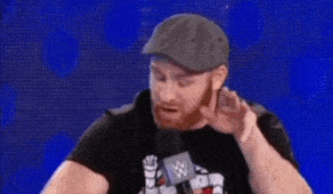 a man with a beard wearing a hat and a t-shirt is sitting in front of a blue background .