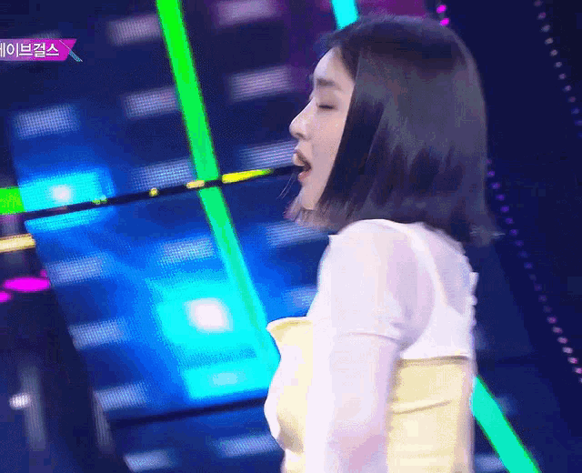 a woman singing into a microphone on a stage with a purple sign that says ' x ' on it