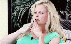 a woman in a green shirt is sitting on a couch covering her face with her hands .