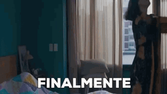 a woman is standing in a bedroom next to a bed and a window with the word finalmente written on it .