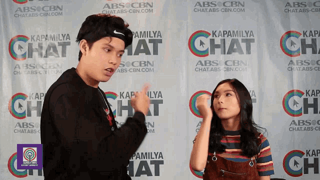a man and a girl are standing in front of a wall that says " kapamilya chat " on it