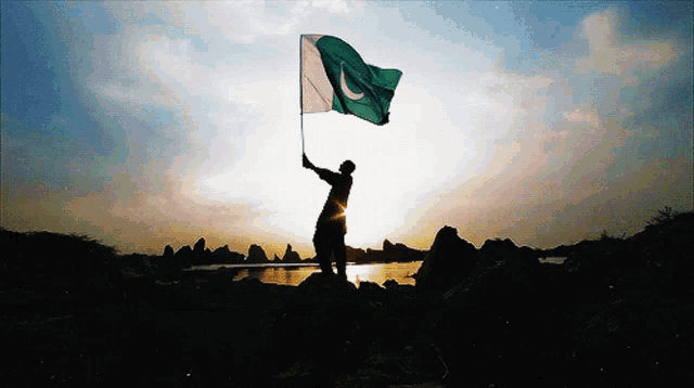 a silhouette of a person holding a flag in front of a lake