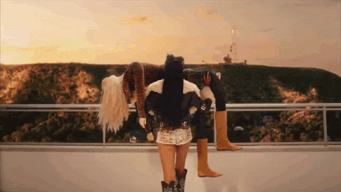 a woman wearing cowboy boots is standing on a balcony with a mountain in the background