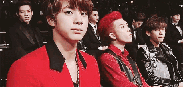 a group of young men sitting in a row with one wearing a red jacket