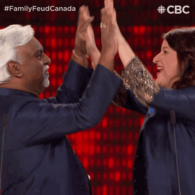 a man and a woman give each other a high five in front of a screen that says family feud canada