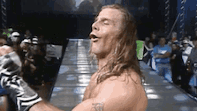 a man with long hair and a tattoo on his arm is standing on a stage .