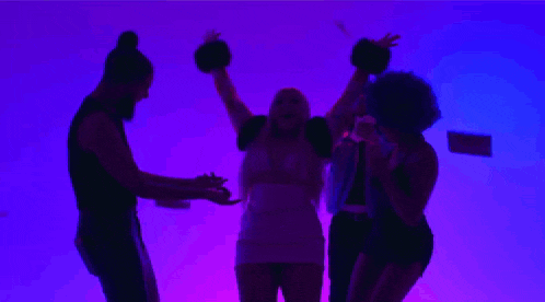 a group of people are dancing in front of a purple background while a woman throws money in the air .