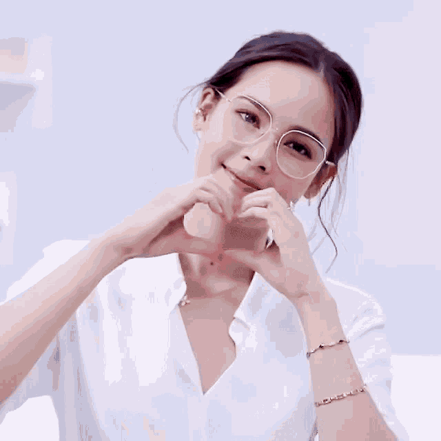 a woman wearing glasses making a heart with her hands