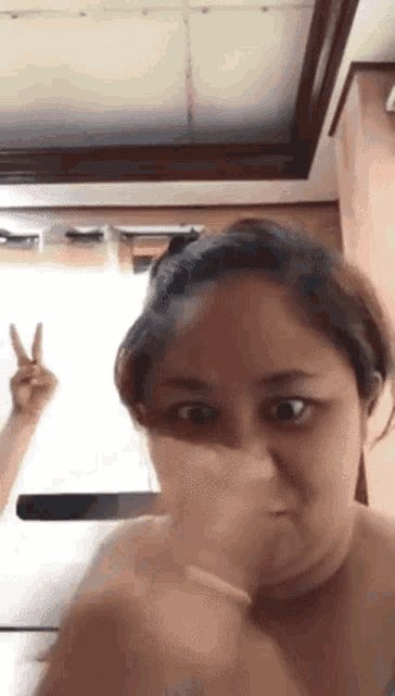 a woman is covering her face with her hand and making a peace sign with her hand .