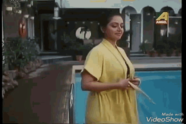 a woman in a yellow robe is standing next to a swimming pool holding a badminton racket .