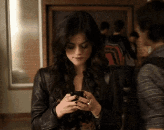 a woman in a leather jacket looks at her cell phone