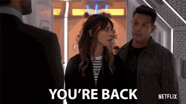 a man and a woman are standing next to each other and the woman is saying you 're back