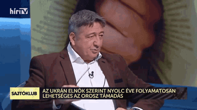 a man in a suit is sitting in front of a screen that says ' hirtv ' on it