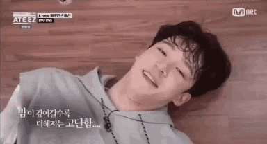 a young man is laying on a wooden floor smiling .