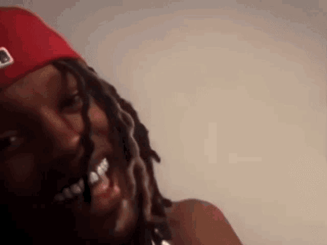 a close up of a person with dreadlocks wearing a red hat and braces .