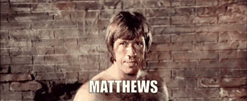 a shirtless man is standing in front of a brick wall with the name matthews written on the bottom .