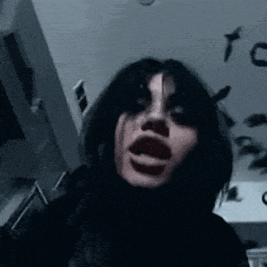 a woman with black hair is making a funny face in a dark room with birds on the ceiling .