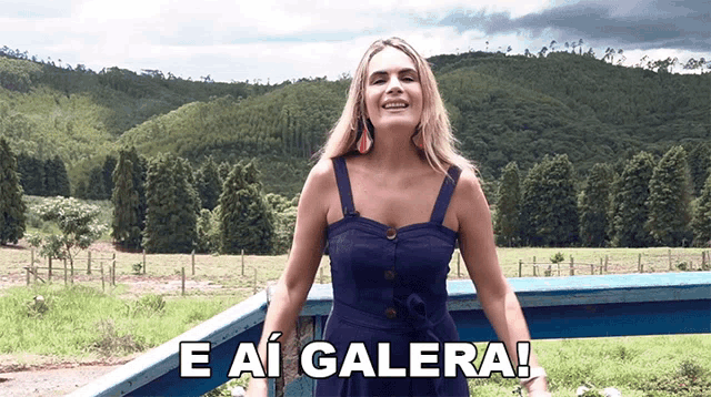 a woman in a blue dress says e ai galera in front of a field