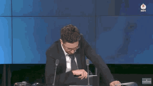 a man in a suit and tie is sitting in front of microphones and says font plaisir a voir