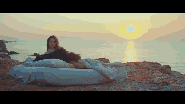 a woman is laying on a bed in front of the ocean