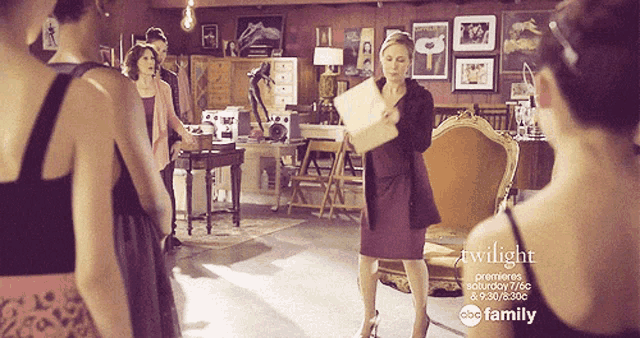 a woman holding a piece of paper in a room with a abc family ad behind her