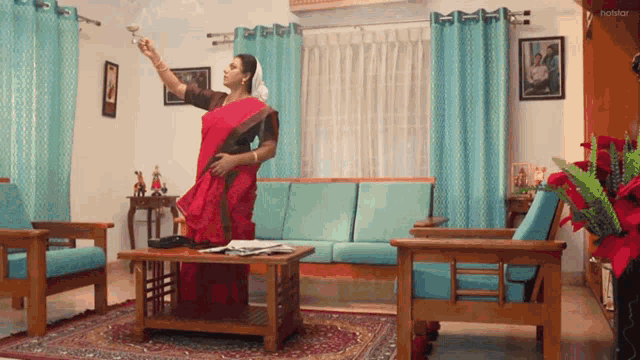 a woman in a red saree is standing in a living room with a couch and chairs