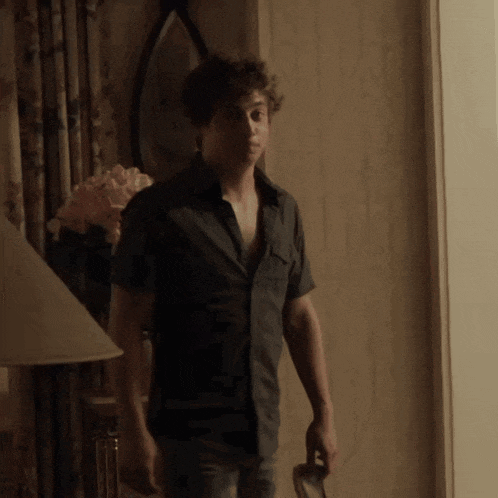 a man in a black shirt is standing in a room with a lamp