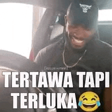 a man wearing a hat and a necklace is sitting in a car laughing .