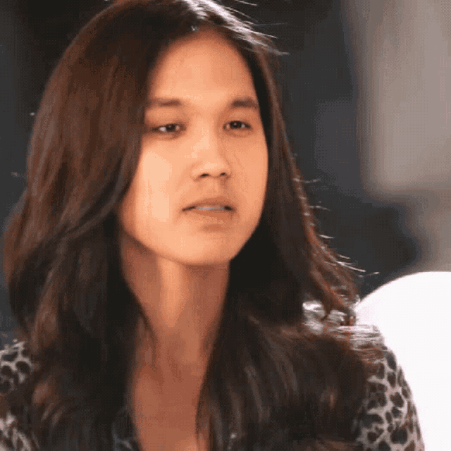 a woman with long hair and a leopard print shirt looks at the camera