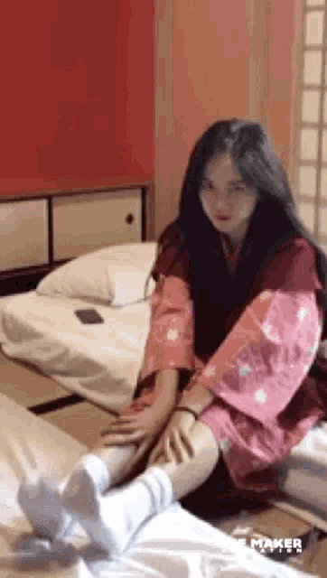 a woman in a kimono is sitting on a bed with her legs crossed .