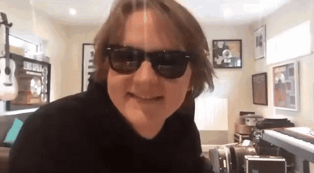 a man wearing sunglasses is making a funny face in a room with a piano .