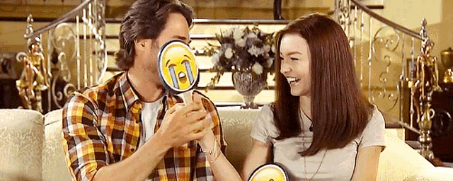 a man and a woman are sitting on a couch holding a lollipop with a smiley face on it