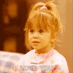 a little girl in a pink shirt is sitting on a couch and saying `` love you '' .