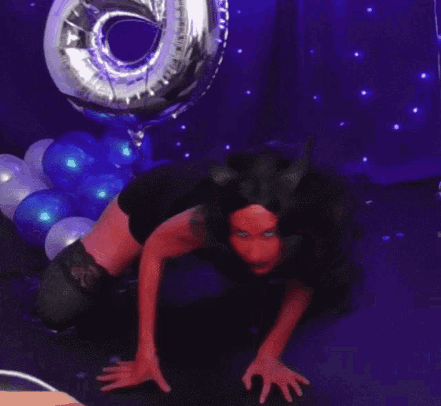 a woman in a devil costume is crawling on the floor in front of balloons