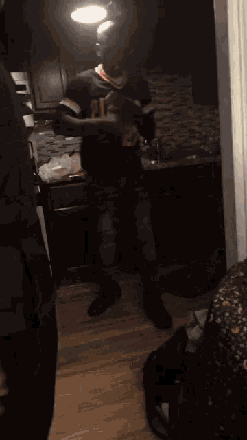 a man in a black jersey with the number 27 on it stands in a kitchen