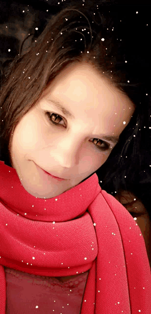 a woman wearing a red scarf looks at the camera with snow falling around her