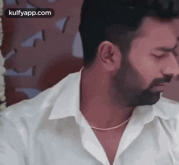 a man with a beard wearing a white shirt and a necklace is looking at the camera .