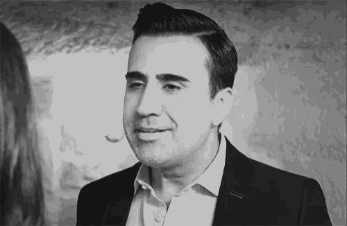 a man in a suit and white shirt is smiling and looking at a woman in a black and white photo .