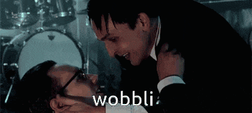 a man in a suit is hugging another man in front of a drum set and the word wobbli is written on the screen .