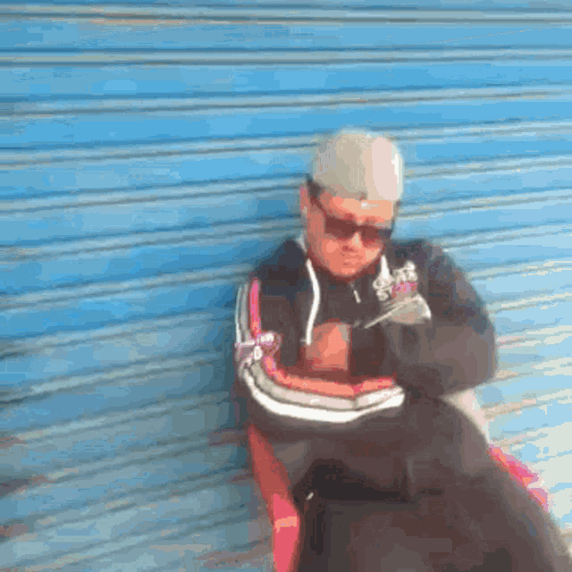 a man wearing sunglasses and a hat is sitting on a bench in front of a blue garage door .
