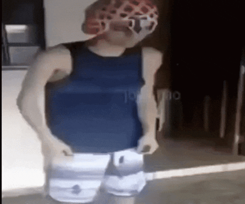 a man wearing a blue tank top and white shorts is standing in front of a door .