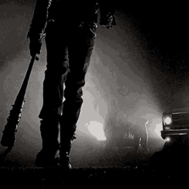 a black and white photo of a person holding a bat in front of a car