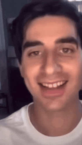 a close up of a man 's face with a white shirt on smiling .